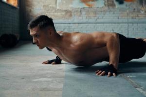 Concentrated young man doing push-up exercises in gym photo