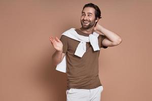 Happy young man looking away and gesturing against brown background photo