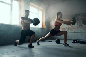 pareja joven en forma que parece concentrada mientras hace entrenamiento con pesas en el gimnasio foto