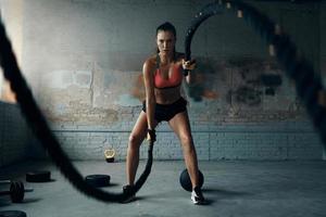 toda la longitud de una hermosa joven haciendo ejercicio con cuerdas de batalla en el gimnasio foto