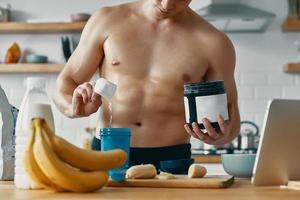 un hombre apuesto que prepara una bebida proteica mientras está de pie en la cocina foto