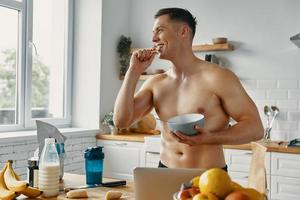 Happy fit man enjoying healthy food while standing at the kitchen photo