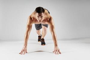 Concentrated fit man preparing to run while standing in starting position against white background photo