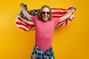 Excited young man carrying American flag while standing against yellow background photo