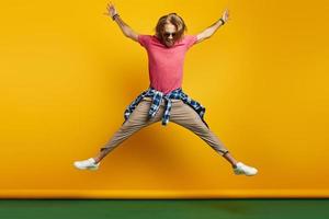 Fashionable young man looking excited while jumping against yellow background photo