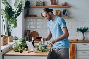 Handsome young man pouring some olive oil on salad while preparing food at the kitchen photo