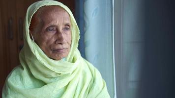 Elderly woman wears a hijab and looks out a window video