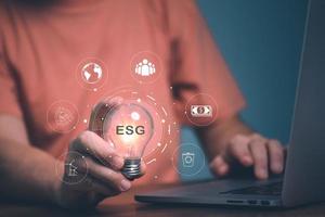 ESG concept, Man hand holding light bulb with ESG icon for environmental, social, and governance in sustainable and ethical business on the Network connection. photo