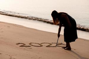 2023 feliz año nuevo, joven mujer sana escribiendo el número 2023 en la playa de arena al amanecer, atención médica, seguro médico, concepto de vida saludable. foto