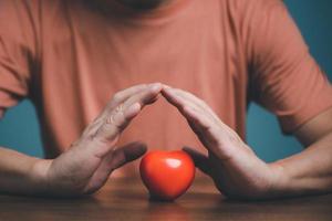 Hands holding and protect red heart for love, health care, organ donation, world heart day, world health day, mindfulness, well being, family insurance concept. photo