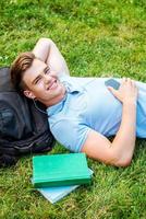 Man relaxing on grass. Top view of handsome young man holding hand behind head and smiling while lying on grass and listening to MP3 Player photo