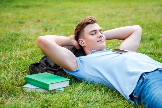 Finding a peaceful place to relax. Handsome young man holding hands behind head and smiling while lying on grass and listening to MP3 Player photo