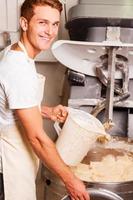 The best dough for our pastry. Confident young man in apron pushing button on dough mixing machine and smiling photo