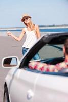 Woman hitching a ride. Beautiful young funky woman hitch-hiking on the side of the road with car on foreground photo