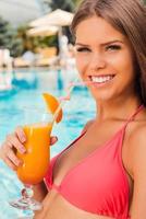 refrescante con cóctel frío. bella joven en bikini sentada junto a la piscina y bebiendo un cóctel foto