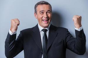 Successful businessman. Happy mature man in formalwear gesturing and smiling while standing against grey background photo