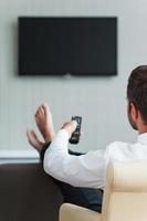 Watching TV in hotel. Rear view of man in white shirt watching TV and holding remote control in hand photo