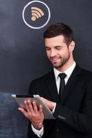 Surfing the internet. Handsome young man working on digital tablet while standing against sharing  symbol chalk drawing on blackboard photo