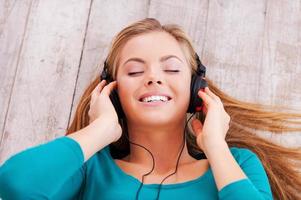 profundamente en la música. vista superior de una hermosa joven tendida en el suelo en su apartamento escuchando música a través de auriculares foto