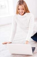 Warmness and comfort. Beautiful young woman sitting on the floor at her apartment working on laptop photo