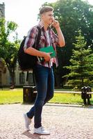 Staying in touch with friends. Full length of handsome male student talking on the mobile phone and smiling while walking outdoors photo