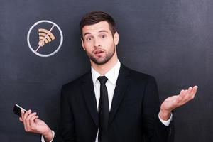 No connection. Frustrated young man holding telephone and looking surprised because of bad connection while standing against sharing  symbol chalk drawing on blackboard photo