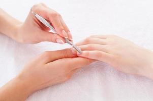 Preparing for manicure. Close-up of beautician cleaning nails of female customer photo