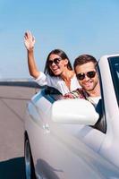 Enjoying their road trip. Happy young couple enjoying road trip in their white convertible photo