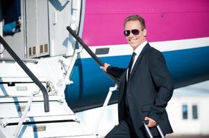 Business calling. Confident mature businessman moving up by airplane ladder to the entrance photo