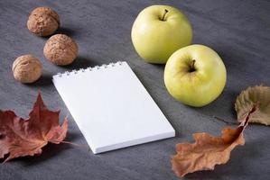 Autumn composition of dry leaves, apples, walnuts white notepad. photo