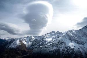 Mountain range, steep snow-covered rocky slopes and peaks and large bizarre cloud photo