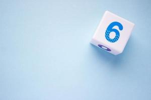 Close-up photo of a white plastic cube with a blue number 6 on a blue background in the upper right corner. With copy space