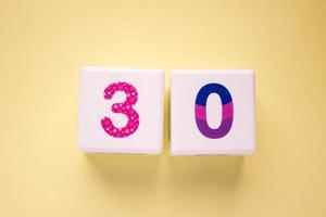 Close-up photo of a white plastic cubes with a colorful number 30 on a yellow background. Object in the center of the photo