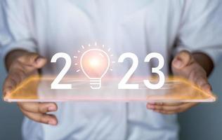 Woman holding 2023 icon and light bulb. Represents the goal setting for 2023, concept of initiation, educational planning, development strategy, educational goal setting. photo