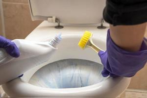 las manos de las mujeres lavan el inodoro en el baño con detergente, un cepillo foto