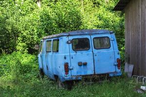 An old broken down abandoned car of blue color standing among the greenery