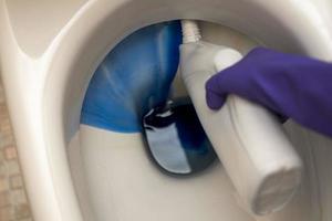 lavar la taza del inodoro en el baño con detergente y guantes de goma foto