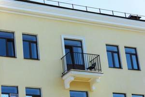 A small cute balcony with a chair on the facade of a yellow residential building, summer photo