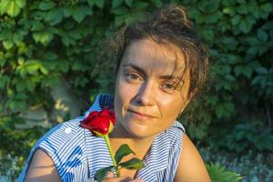 Portrait of a young beautiful woman with a rose flower in her hands, a blue and white dress on a green background photo