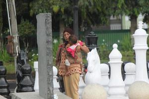 Magelang, Indonesia, 2022 - photo of an old mother holding her child on the edge of the park in the afternoon