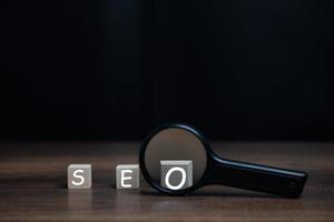 lupa con bloque de madera seo, optimización de motor de búsqueda, seo, tecnología para teléfono móvil, teléfono inteligente, computadora, página web, sitio web, ranking de medios sociales y velocidad. foto