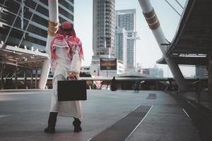 hombre de negocios árabe con un sueño inspirador sosteniendo un maletín, parado en la ciudad, vista trasera, espacio para copiar. foto