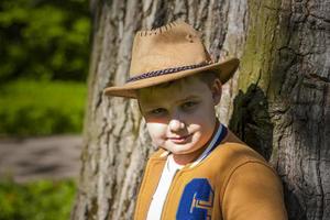 Cute boy posing in a cowboy hat in the woods by a tree. The sun's rays envelop the space. Interaction history for the book. Space for copying photo