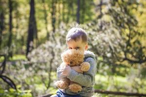 A cute boy is playing with a bear cub in the forest. The sun's rays envelop the space of the clearing with a stump. A magical story of interactions for the book. Space for copying. Selective photo