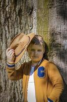 Cute boy posing in a cowboy hat in the woods by a tree. The sun's rays envelop the space. Interaction history for the book. Space for copying photo