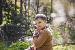 A cute young man is sitting and posing in a clearing in the forest. The sun's rays envelop the space of the clearing with a stump. Space for copying. photo