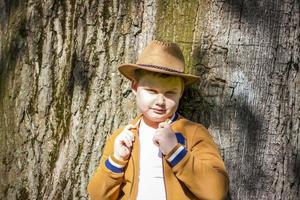 Cute boy posing in a cowboy hat in the woods by a tree. The sun's rays envelop the space. Interaction history for the book. Space for copying photo