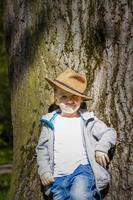 Cute boy posing in a cowboy hat in the woods by a tree. The sun's rays envelop the space. Interaction history for the book. Space for copying photo