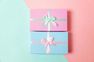 Small gift box wrapped pink and blue paper isolated on blue and pink pastel colorful trendy geometric background. Christmas New Year birthday valentine celebration present romantic concept. photo