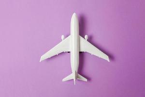 simplemente diseño plano, modelo de juguete en miniatura, avión sobre fondo de moda de papel de colores pastel púrpura violeta. viaje en avión vacaciones fin de semana de verano viaje de aventura en el mar billete de viaje concepto de viaje. foto